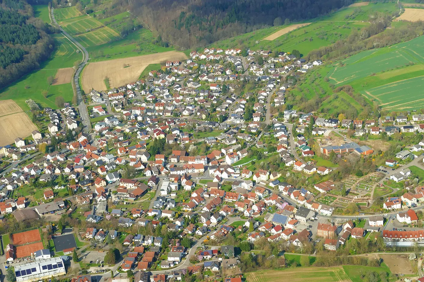 Luftbild der Ortsmitte von Wiesenbach von Süden nach Norden. Das Rathaus ist der hellrote Bau mit Türmchen …