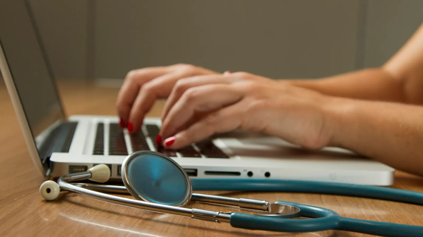 Person mit Stethoskop arbeitet am Laptop