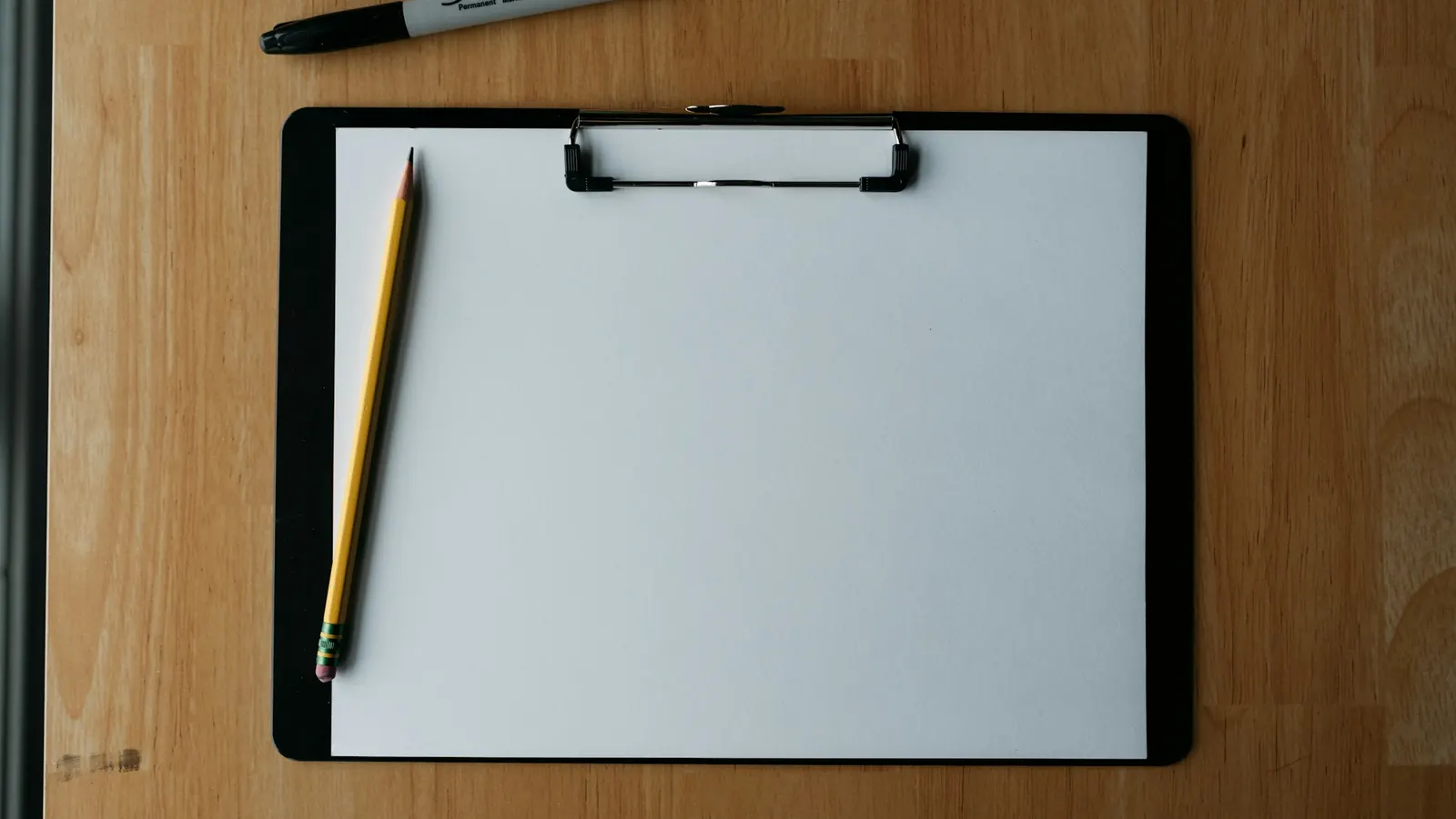 Klemmbrett mit leerem Blatt und Bleistift auf einem Holztisch